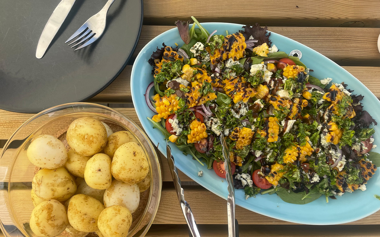 Tre tallrikar på ett bord. En tom tallrik, en tallrik med färsk postatis och en tallrik med sallad gjord på grillad majs och gorgonzola.